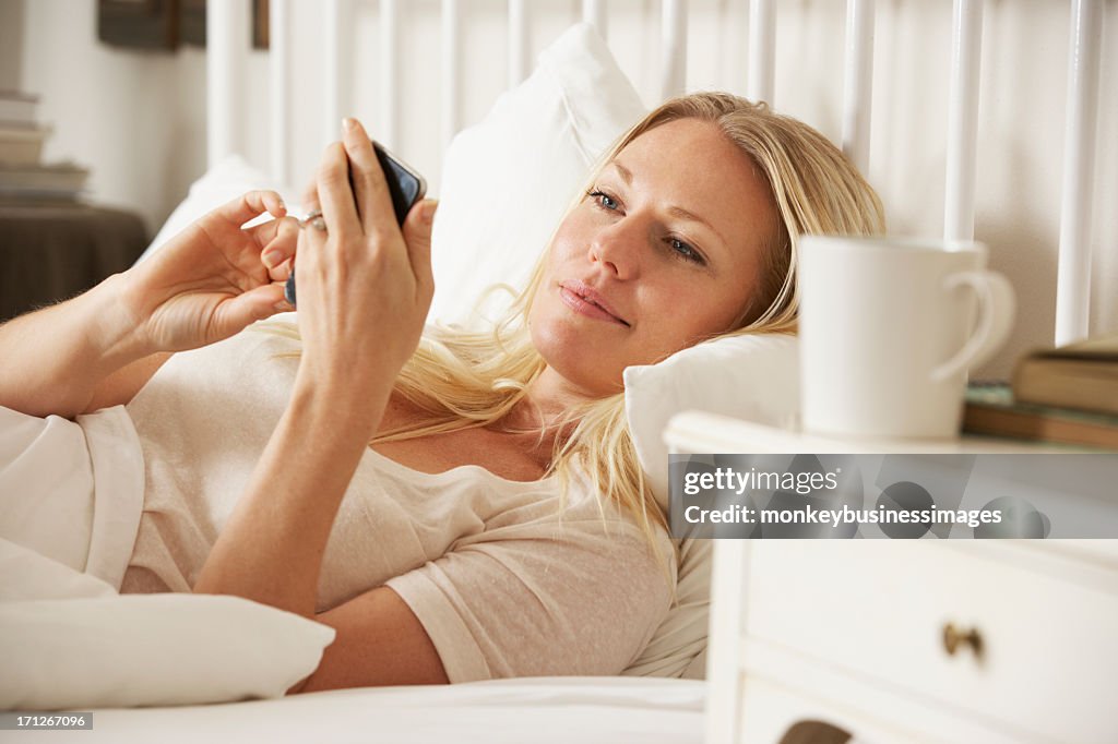 Woman In Bed At Home Texting On Mobile Phone