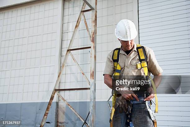 arbeiter putting auf sicherheitsgurt - sicherheitsausrüstung stock-fotos und bilder