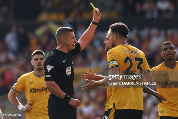 English referee Robert Jones shows a yellow card to Wolverhampton Wanderers' English defender Craig Dawson during the English Premier League football...