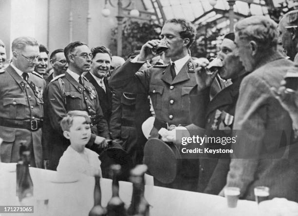 King Leopold III of Belgium has a drink at the buffet whilst Prince Baudouin looks on. The party is being given by the King at the Royal Palace of...