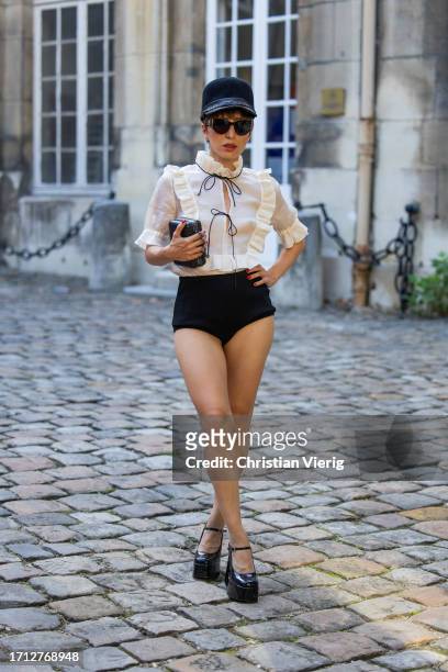 Salome Chaboki wears black hat, ruffled blouse, black shorts, bag outside RDNT Andre Tan during the Womenswear Spring/Summer 2024 as part of Paris...