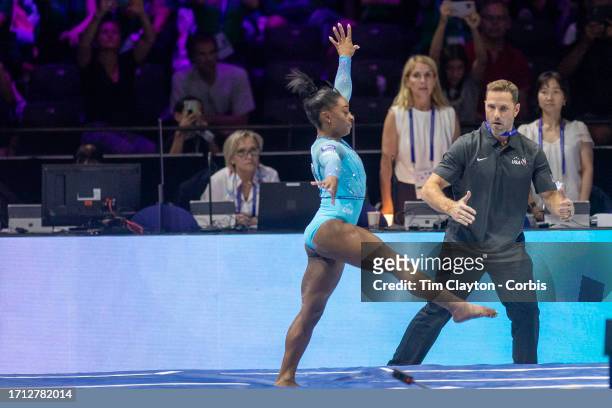 October 01: Simone Biles of the United States lands her Yurchenko double pike vault with coach Laurent Landi on the vault mat for assistance during...