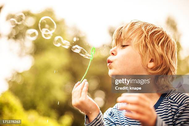 cute little boy outdoors blowing bubbles - bellenblaas stockfoto's en -beelden