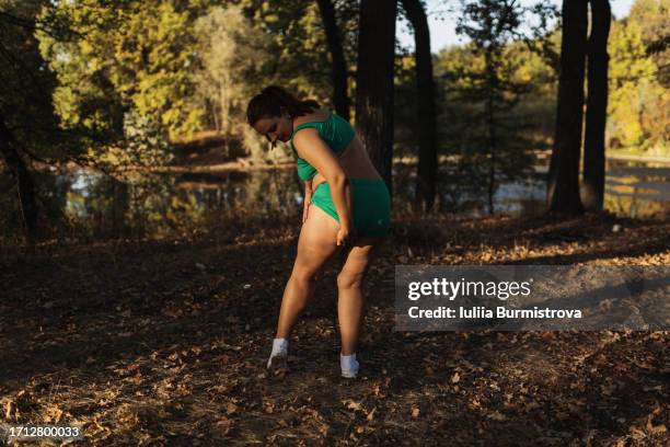 standing by tranquil river full-bodied woman in revealing sports clothes examines plump thigh - man standing full body stock-fotos und bilder