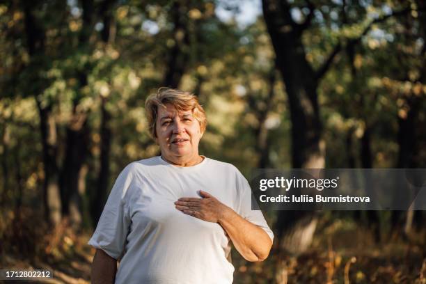 blonde elderly woman renewing strength after vigorous jog on footpath in forest - sin aliento fotografías e imágenes de stock