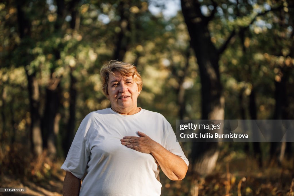 Blonde elderly woman renewing strength after vigorous jog on footpath in forest