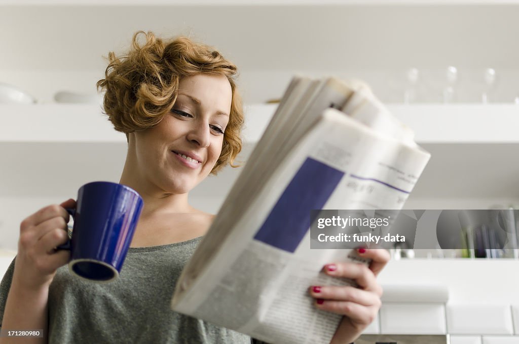 Junge Frau mit Kaffee und Tageszeitung