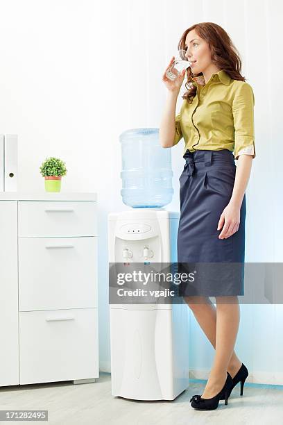 businesswoman having drink from water cooler - water cooler stockfoto's en -beelden