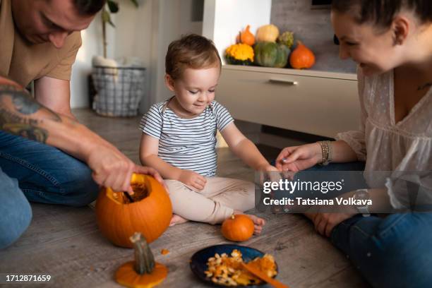 joyful mother playing with cute toddler while skillful husband scooping out pumpkin seeds while making halloween decorations - camisa castanha imagens e fotografias de stock