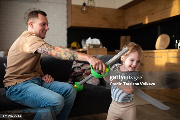 playful father and adorable toddler son engage in friendly sword fight with plastic swords - toy sword stock pictures, royalty-free photos & images