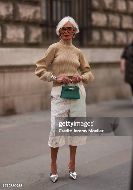 Grece Ghanem is seen outside Hermes show wearing chunky golden earrings, oversized orange colored sunnies, beige striped turtle neck, silver white...