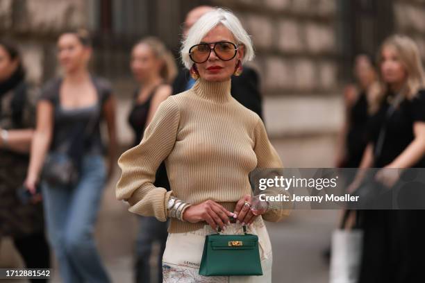 Grece Ghanem is seen outside Hermes show wearing chunky golden earrings, oversized orange colored sunnies, beige striped turtle neck, silver white...