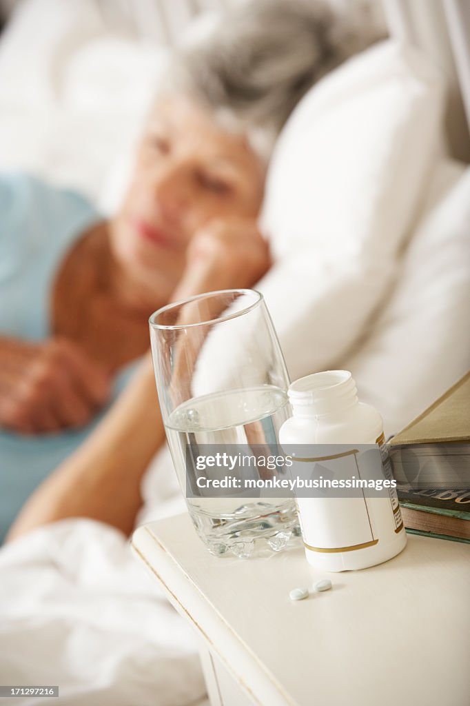 Medication On Bedside Table Of Sleeping Senior Woman