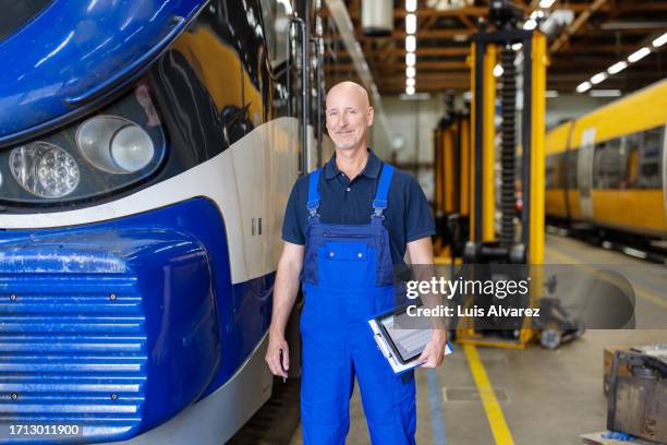 portrait of mature man standing by train locomotive in maintenance workshop - kontrollinspektoren stock-fotos und bilder
