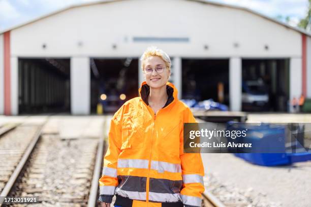 portrait of woman train engineer in safety vest standing on rail tracks at the railway depot - machinist stockfoto's en -beelden