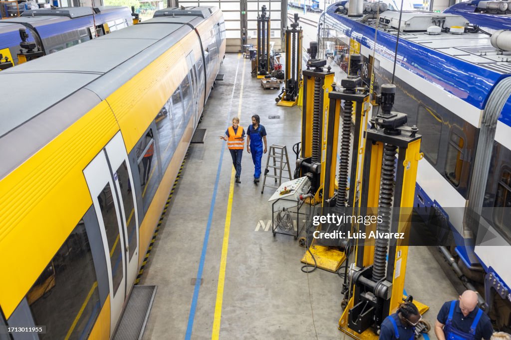 High angle view of railway engineers walking by the train and discussing maintenance tasks at workshop