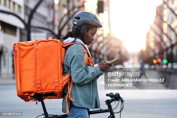 a young delivery woman on her bicycle looking on her smartphone for the route of her delivery - bike messenger stockfoto's en -beelden