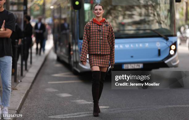 Guest is seen outside Hermes show wearing rose gold long earrings, orange and black checkered Hermes jacket with silver details and matching short...