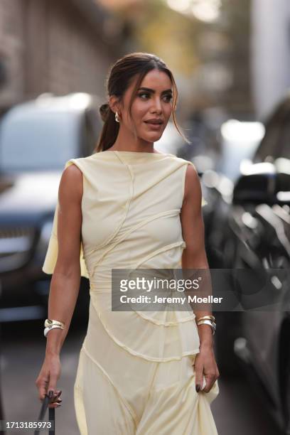 Camila Coelho was seen wearing a light yellow dress, a silver bracelet, golden earrings and a black bag with yellow gold ornaments on it before the...