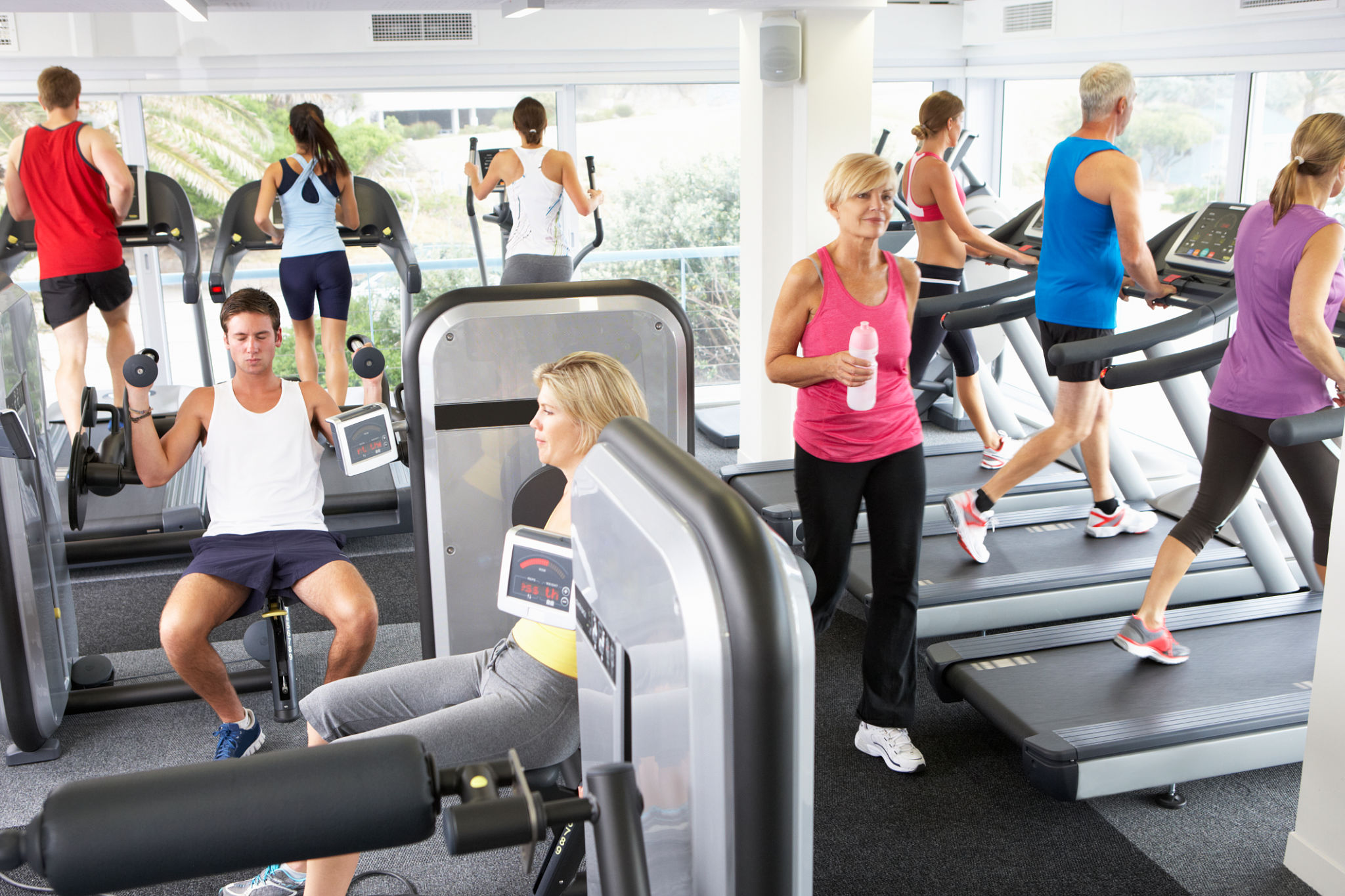 Elevated View Of Busy Gym With People Exercising On Machines Elevated View Of Busy Gym With People Exercising On Machines