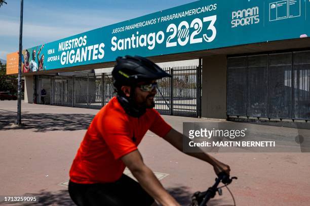 Cyclist passes by the National Stadium where a banner advertising the upcoming Pan American Games Santiago 2023 is displayed, in Santiago on October...