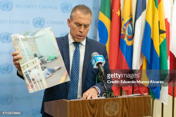 Israel's Ambassador to the U.N. Gilad Erdan holds up a picture showing people killed by Hamas members as he speaks to reporters during a stakeout...