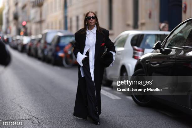 Fashion Week guest was seen wearing oversized black pants, a big black coat and an oversized white shirt with collar, a black bag and dark shades as...