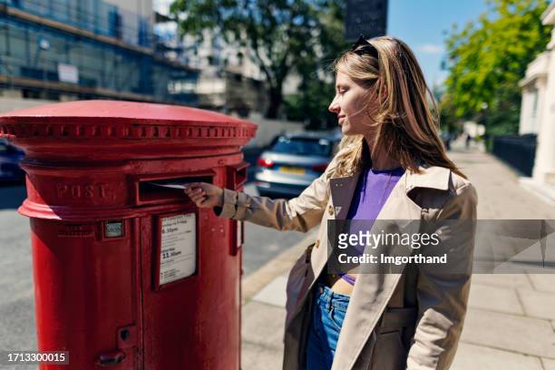 teenage girl sending a postcard from london, united kingdom - brievenbus stockfoto's en -beelden
