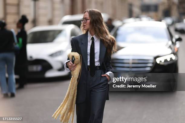 Fashion Week guest was seen wearing an oversized grey suit, transparent shades, a white shirt with collar, a black tie and a yellow Bottega Veneta...