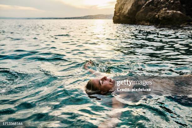 hembra adulta joven flotando, relajándose en las cálidas aguas de la costa azul en el sur de francia durante sus vacaciones. - flotar sobre agua fotografías e imágenes de stock