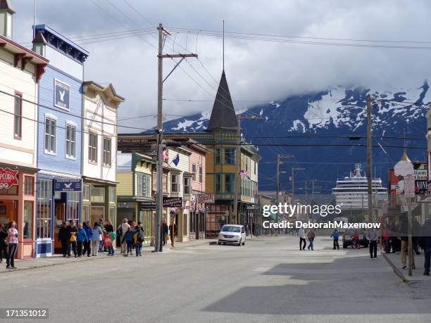 downtown skagway tourists with snow and cloud covered mountains background - skagway alaska stock pictures, royalty-free photos & images