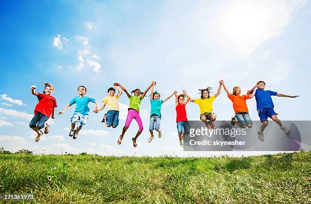 gruppe von kindern spaß und springen gegen den himmel. - holding hands kids stock-fotos und bilder
