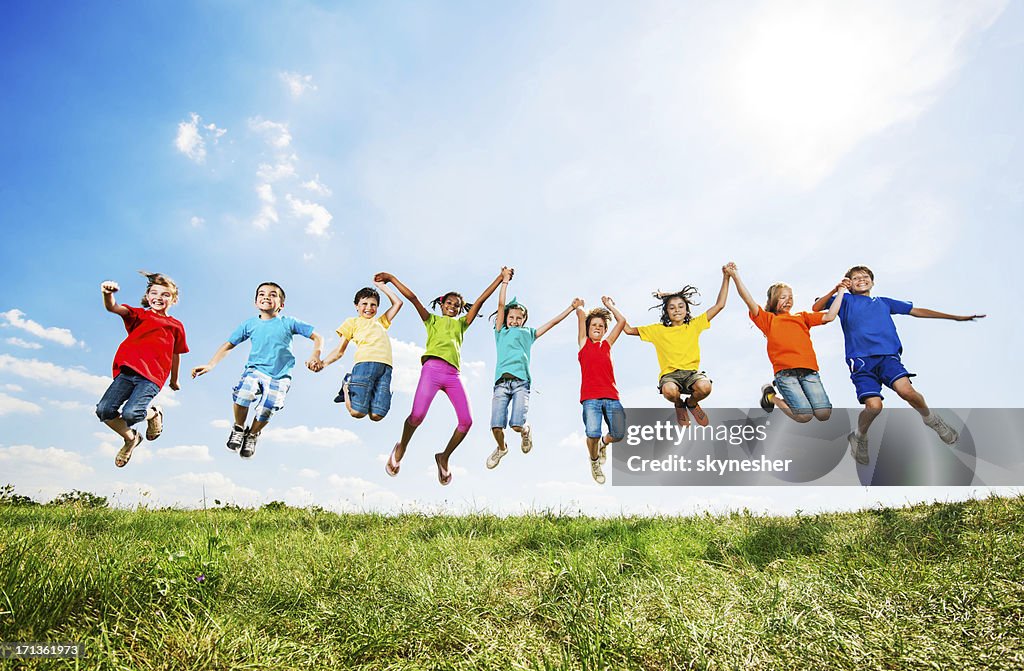 Grupo de niños divirtiéndose mientras salto contra el cielo.