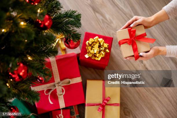 mujer colocando un regalo debajo del árbol de navidad - debajo de fotografías e imágenes de stock