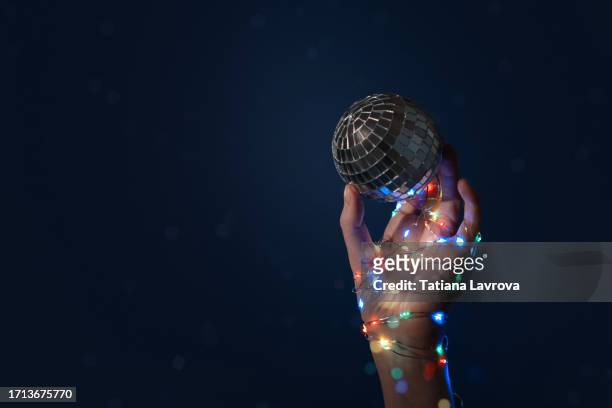 beautiful female hand with natural manicure wrapped in colorful garland with bokeh lights holding shiny christmas toy - silver disco ball. xmas, preparing for the new year's celebration, birthday concept. - silver disco ball stock pictures, royalty-free photos & images