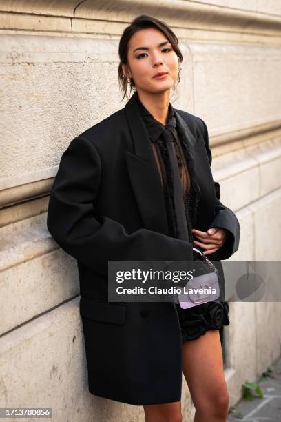 Guest wears a black sheer mini dress with roses details, black coat and lilac Valentino bag, outside Valentino, during the Womenswear Spring/Summer...