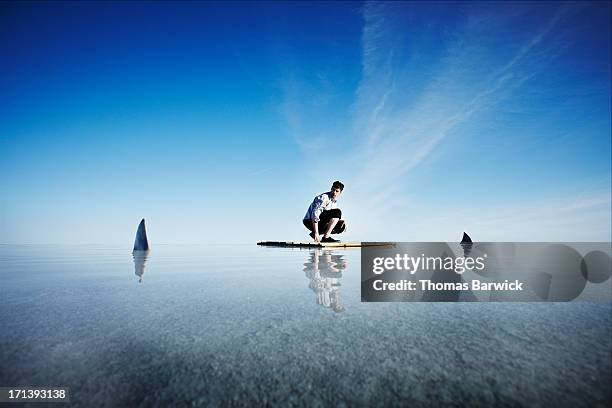 businessman kneeling on life raft watching sharks - shark fin stock-fotos und bilder