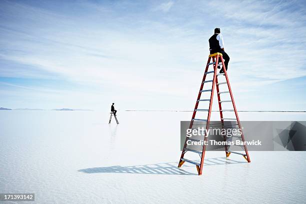 businessmen sitting on two different sized ladders - rivaliteit stockfoto's en -beelden