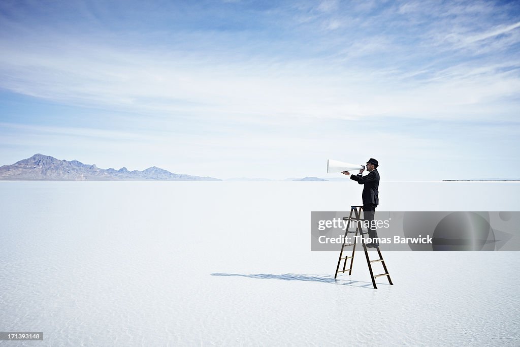 Businessman with megaphone on ladder in lake