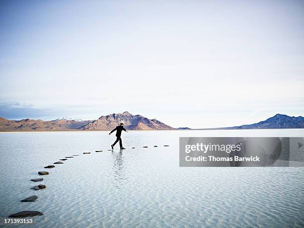 businessman leaping between stones on pathway in l - stone concept stockfoto's en -beelden