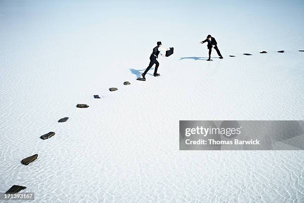 businessmen trying to pass briefcase across gap - cohesion stock-fotos und bilder