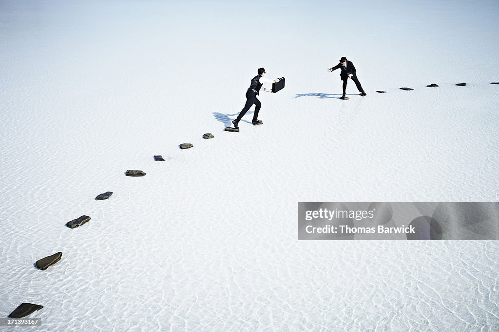 Businessmen trying to pass briefcase across gap