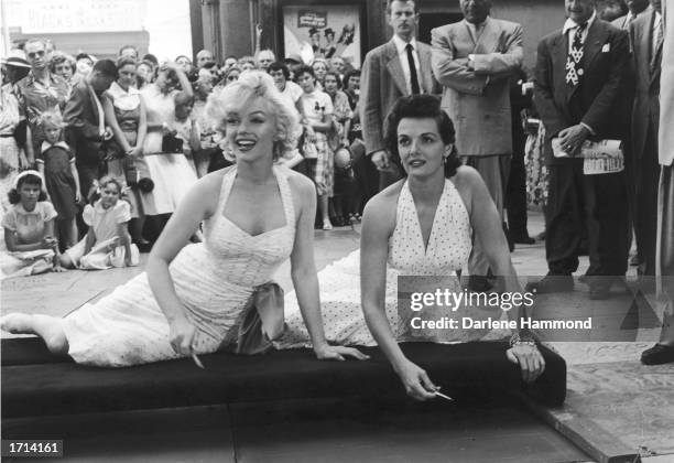 American actresses Marilyn Monroe and Jane Russell sit on a cushion and prepare to sign their foot and hand prints in the cement in front of...