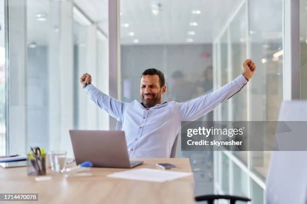 entrepreneur masculin épuisé s’étirant tout en travaillant sur un ordinateur portable au bureau. - les-bras-écartés photos et images de collection