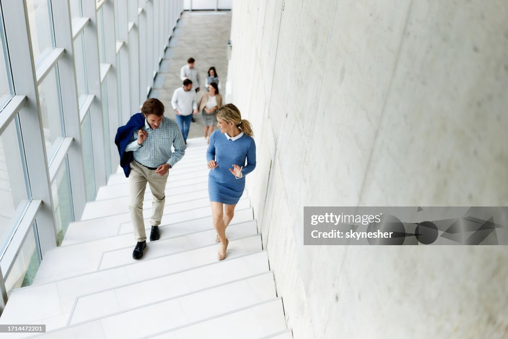 Happy business colleagues talking while walking up the stairs in a hallway.