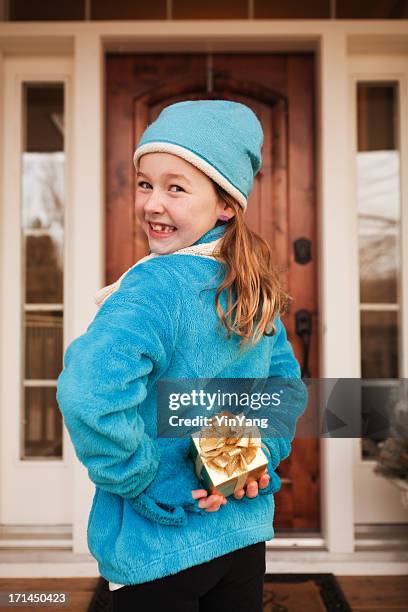 little girl with surprise christmas gift visiting friend - hiding behind back stock pictures, royalty-free photos & images