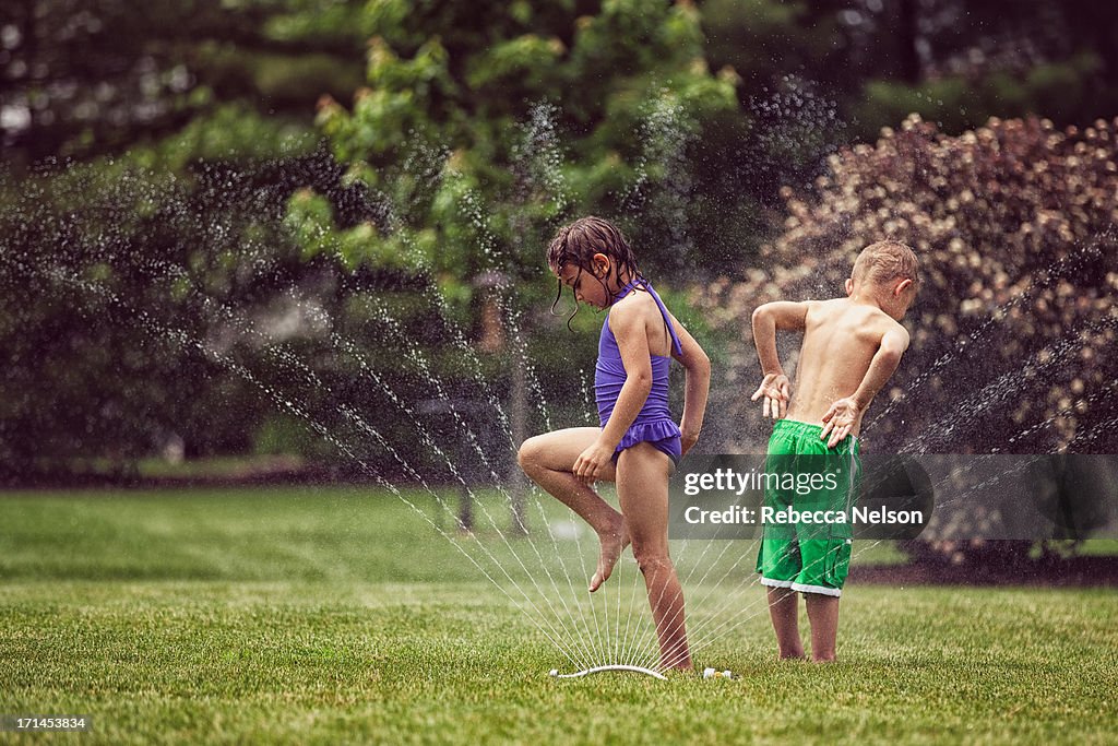 Boy and girl cooling off in garden sprinkler