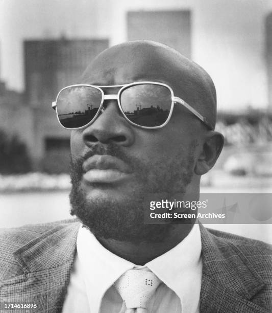 Isaac Hayes, American Soul singer, composer and actor poses in sunglasses against city backdrop for the 1974 thriller 'Three Tough Guys'.