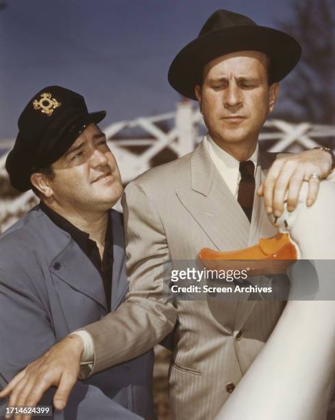 Legendary comedy duo Bud Abbott and Lou Costello clown around at amusement park in a color portrait, 1950s.