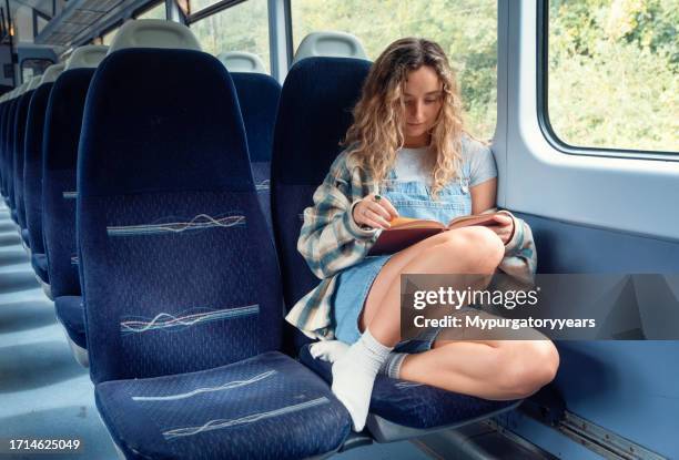 a young woman reading a book on a commuter train - feet up stock pictures, royalty-free photos & images